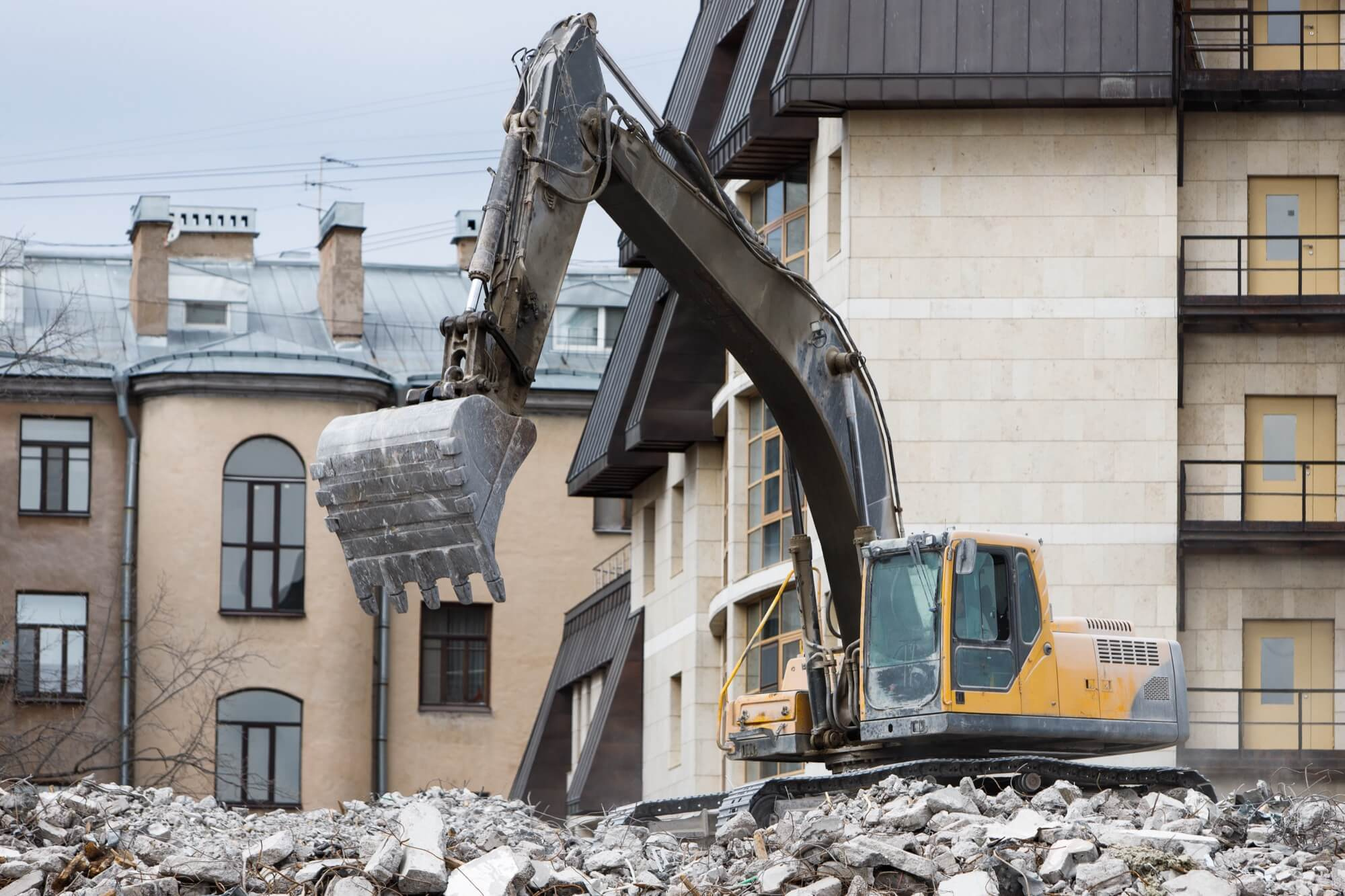 En stor grävmaskin står på en omfattande hög av betongrester och rivningsmassor på en byggarbetsplats för rivning.