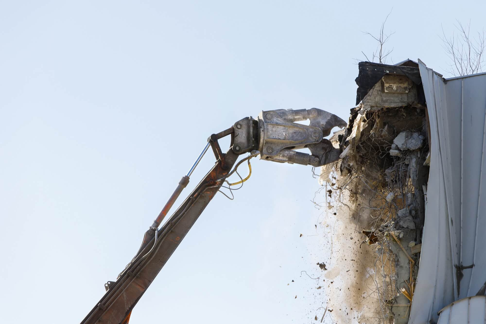 En kraftfull hydraulisk sax på en grävmaskinsarm som krossar en betongkonstruktion under en tung rivning.