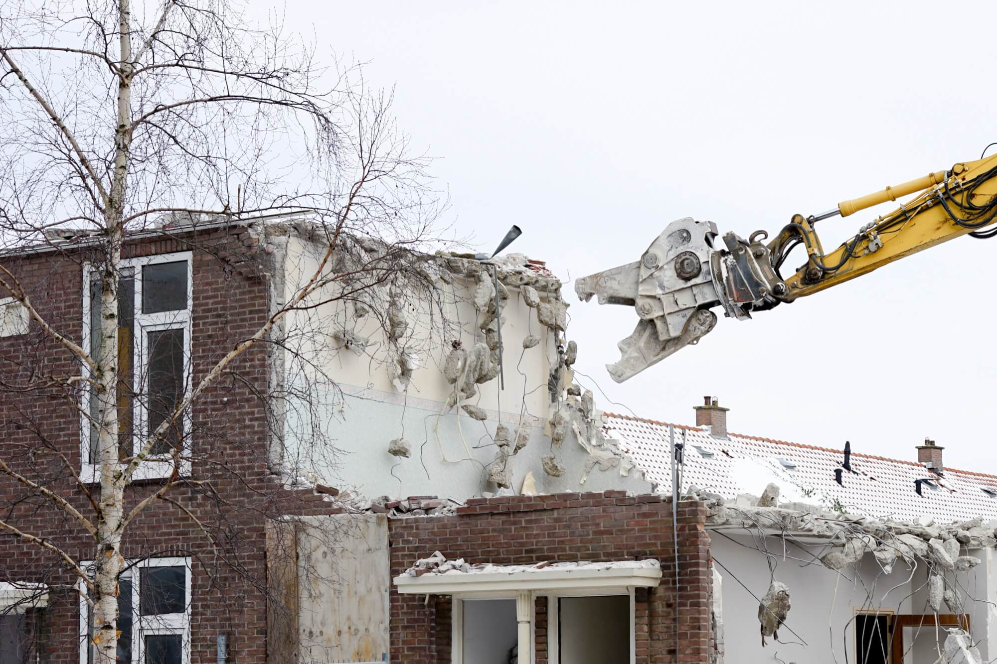 En grävmaskin använder en betongsax för en kontrollerad rivning av ett bostadshus i tegel.